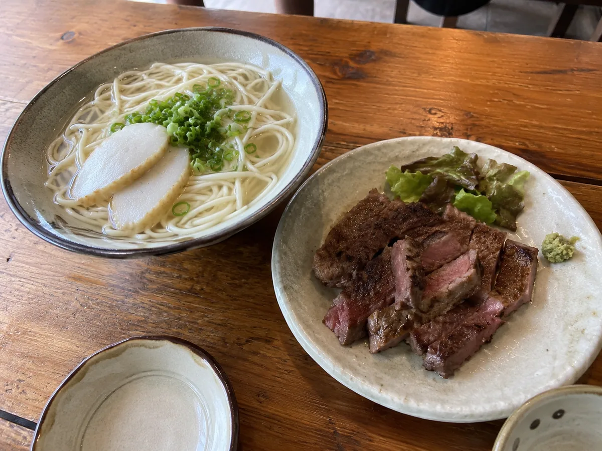 木のテーブルに並んだ、丸い麺のあっさりした汁そばと焼いた牛肉の皿